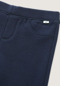 Pantalones de chándal azul marino en un material suave con una cinturilla elástica ancha, bolsillos laterales y una pequeña etiqueta circular de la marca.