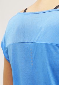 Blue athletic shirt with short sleeves, made of lightweight fabric. Features a smooth texture and small circular accents on the back.