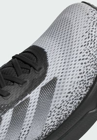 Schwarze und weiße Sneaker mit einem strukturierten Mesh-Obermaterial, schwarzen Schnürsenkeln und drei hervorgehobenen schwarzen Streifen an der Seite.