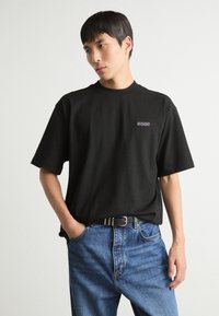 Tricou din bumbac negru cu mâneci scurte, guler rotund, având brodat logo-ul "BOSS" pe pieptul stâng; asortat cu blugi de denim albaștri.