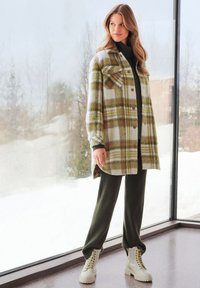 Geruit shacket in groene en gele tinten, met knoopsluiting, borstzakken, gecombineerd met geribbelde donkergroene broek en beige combatlaarzen.