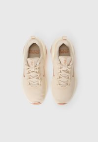 Een paar beige Nike hardloopschoenen met mesh-stof, veters en een beige zool, gezien van bovenaf op een witte achtergrond.