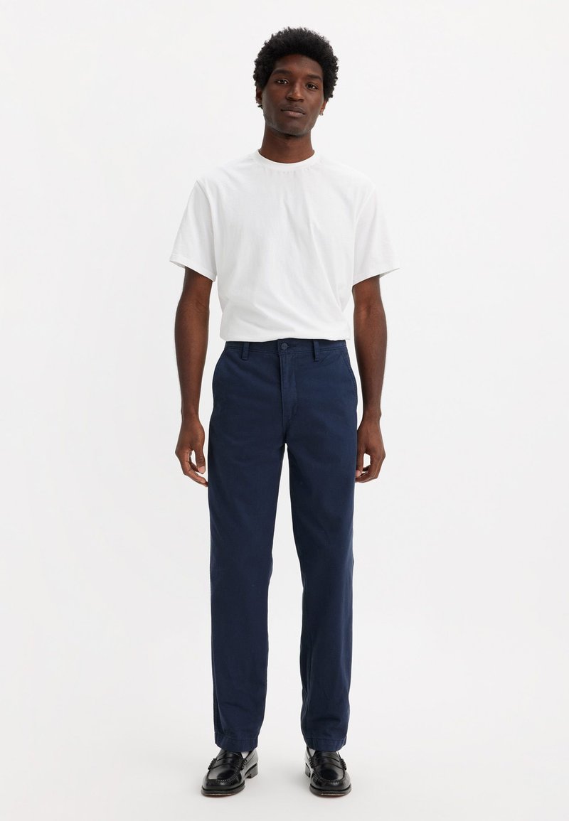Chinos azul marino con un diseño de pierna recta, combinados con una camiseta blanca lisa; ambos confeccionados en tela de algodón. Textura suave, acentos sencillos.