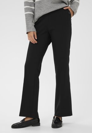 Pantalons évasés noirs avec une texture lisse et une taille ajustée. Comprend deux boutons extérieurs à la taille. Associés à des mocassins noirs brillants.