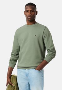 Sudadera verde de algodón con pu�ños acanalados y cuello redondo, con un pequeño logo bordado en el pecho, combinada con vaqueros azul claro.