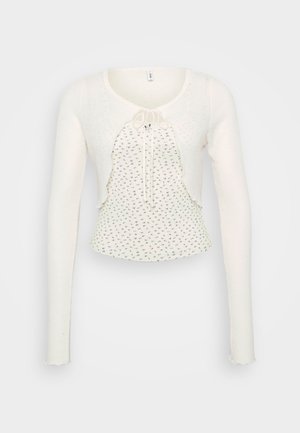 Maglione bianco a maniche lunghe con scollatura rotonda, tessuto strutturato, chiusura anteriore con fiocco e orlo ondulato caratterizzato da piccoli motivi floreali.