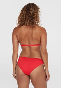Červený bikini s bandeau topom a zodpovedajúcim vysokým pásom, hladká textúra a minimálne detaily na zadnej strane.