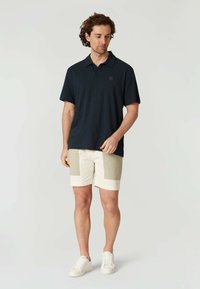 Námornická polo košile z lehkého materiálu, kombinovaná s krémovými šortkami s béžovými prvky a bílými teniskami. Příležitostný a funkční design.