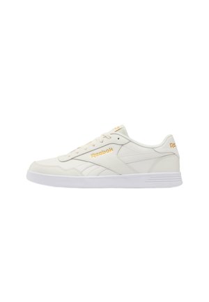 Lage off-white Reebok sneaker met witte zool, veterfront en gouden Reebok-logo op zijkant, hiel en tong.