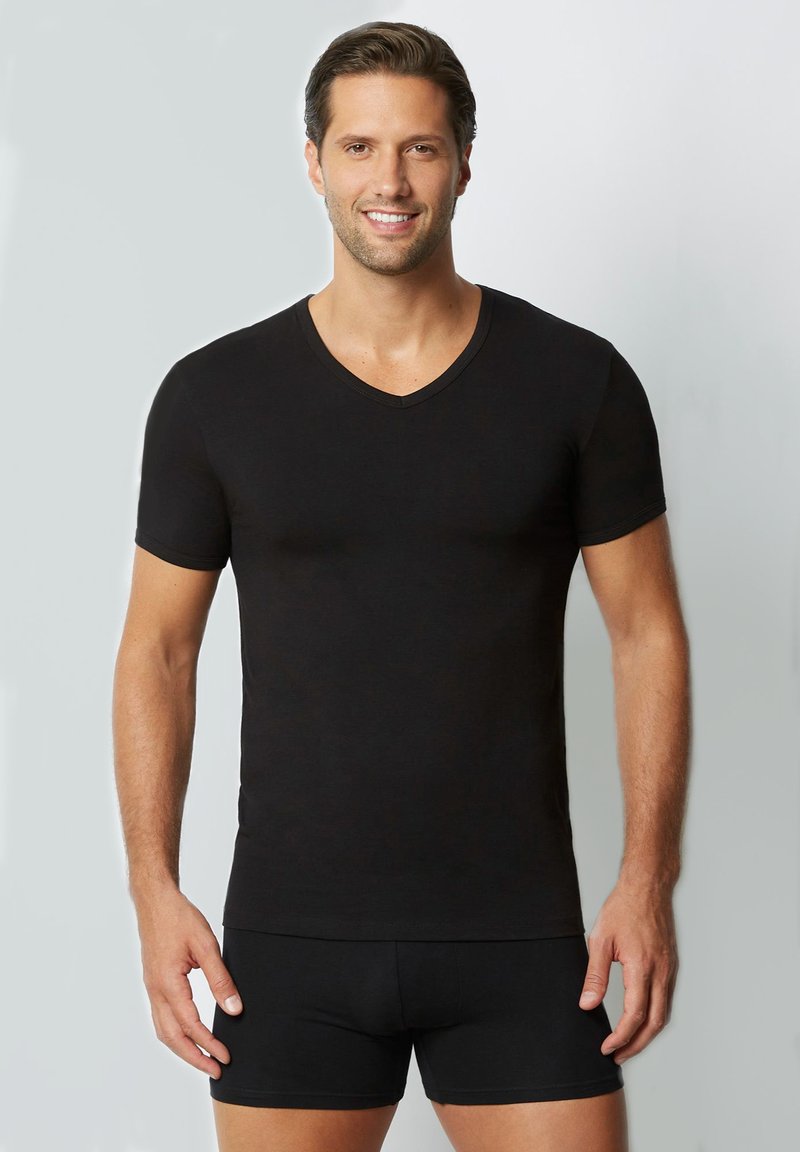 T-shirt nero a maniche corte con scollo a V, realizzato in tessuto liscio, design aderente, con una texture morbida e dettagli di cucitura sottili. Indossato con pantaloni corti neri abbinati.
