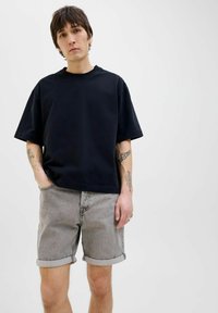 T-shirt noir à manches courtes associé à un short en denim gris. Le short a des ourlets retroussés et une finition texturée. Fond uni.