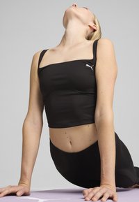 Melna sporta kroppa topa ar kvadrātveida kakla izgriezumu un plānām siksnām, ar nemanāmu logo kreisajā pusē un elegantu dizainu.