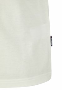 Lichtgekleurde textuurshirt met een ronde onderkant en een klein merkje aan de zijkant. De stof lijkt ademend en casual.