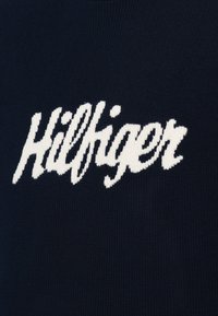 Granatowy dzianinowy wyrób z białym haftowanym napisem "Hilfiger" w kursywie. Tekstura jest gładka z jednolitym splotem.