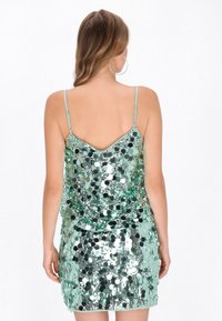 Flitteres ruha állítható spagetti pántokkal, csillogó zöld anyagból és testhez simuló szabással, amelyet kör alakú flitterek díszítenek.