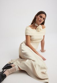 Kreminė ribotuota palaidinė be petnešų su gėlių akcentu, derinama su smėlio spalvos satino sijonu. Juodi aštrūs kulniukai užbaigia įvaizdį.