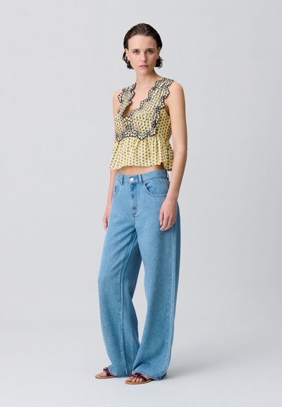Top cropped giallo con motivo floreale nero e bordi arricciati, abbinato a jeans a vita alta blu chiaro e a gamba larga.