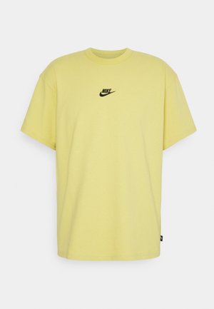 T-shirt jaune manches courtes Nike avec logo noir centré sur la poitrine, présenté sur un fond gris clair.