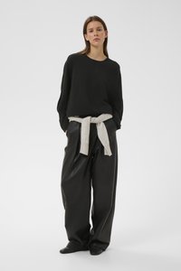 Must suur paheksatud kampsun koos kõrge vöökohaga mustade nahkpükstega. Vöökohale seotud helehall kootud särk lisab kontrasti. Siledad tekstuurid.