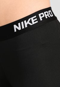 Svarta Nike Pro leggings med en bred svart midja som har vit "NIKE PRO" text. Slät, stretchig tyg med en åtsittande design.