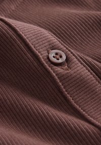 Tissu marron côtelé avec une vue rapprochée d'un détail de bouton. Le bouton est rond, gris clair avec un design à quatre trous, créant un aspect texturé.