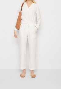 Haut en lin blanc ample à col en V, associé à un pantalon en lin blanc assorti avec une taille élastique. Sandales tressées couleur beige clair.