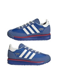 Baskets bleues avec des rayures blanches et des accents dorés. Les caractéristiques incluent une semelle en caoutchouc, une tige texturée et un col rembourré pour plus de confort.