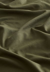 Tissu vert olive, texture lisse, légèrement extensible, avec un léger éclat et un drapé naturel. Des plis et des rides visibles créent de la profondeur.