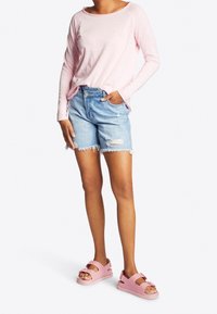 Rosa Langarmshirt, hellblaue Denim-Shorts mit ausgefranstem Saum und rosa Sandalen mit Schnallen-Detail. Lässiges Sommeroutfit präsentiert.
