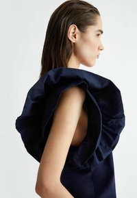 Abito navy con un ampio colletto arricciato, caratterizzato da una superficie liscia e un design senza maniche, che mette in evidenza la spalla e il profilo laterale.