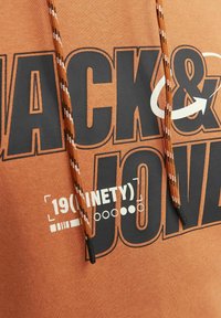 Sudadera naranja con texto en negro en negrita que dice "ACK & JON" y "19(INETY)." Cuenta con cordones con un diseño texturizado y colores contrastantes.