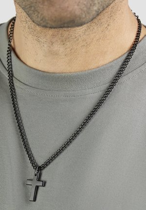 Schwarze Metallkette mit flachem Kreuzanhänger, getragen über einem grauen Hemd. Die Kette weist strukturierte Glieder und eine polierte Oberfläche auf.