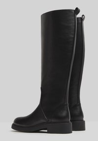 Schwarze knöchelhohe Lederstiefel mit glatter Textur, runder Zehenform und flacher Sohle. Mit Anziehhilfen für einfachen Einstieg.