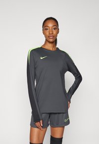 Nike sportska odjeća koja uključuje sivi duksericu dugih rukava s neonsko zelenim detaljima i odgovarajuće kratke hlače. Materijal je gladak i sportski.