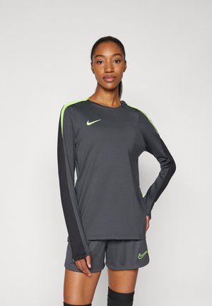 Nike-Sportbekleidung mit einem grauen Langarmshirt mit neon-grünen Akzenten und passenden Shorts. Das Material ist glatt und athletic.