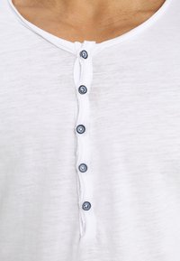 Weißes Baumwollhemd mit einer Knopfleiste und fünf dunkelblauen Knöpfen, lockerer Schnitt und einem weichen, leicht strukturierten Stoff.