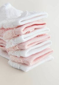 Stabel af foldede bløde lyserøde og hvide strikkede babysokker med blonde detaljer på en lys baggrund.