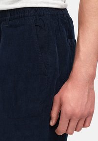 Marineblå kordfløyel bukser med elastisk midje, sidelommer og en myk tekstur. Synlige ribber skaper et tydelig mønster og dybde.