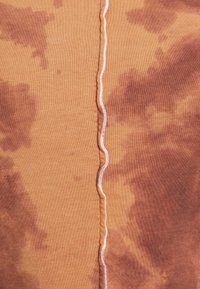 Ribbade tyger i en varm orange med bruna batikmönster. Har en central söm med kontrasterande vit sömnad.