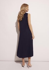 Sukienka bez rękawów, do ziemi, w kolorze granatowym, z dopasowaną górą i zwiewnym dołem. Gładki materiał i minimalizm w detalach.