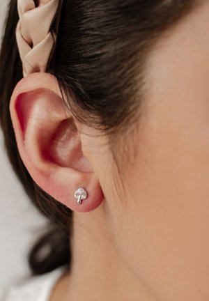 Silver stud earring shaped like a mushroom, featuring a textured cap and a smooth stem, set against a close-up of a human ear.