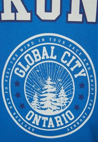 Tissu bleu avec texte blanc « GLOBAL CITY ONTARIO » entourant des pins et des rayons, entouré d'étoiles et d'une phrase motivante.