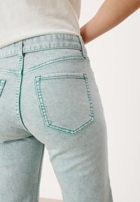 Los vaqueros de mezclilla azul claro presentan bolsillos cosidos, una cintura alta y un acabado texturizado, con detalles de hilo en contraste a lo largo de las costuras.