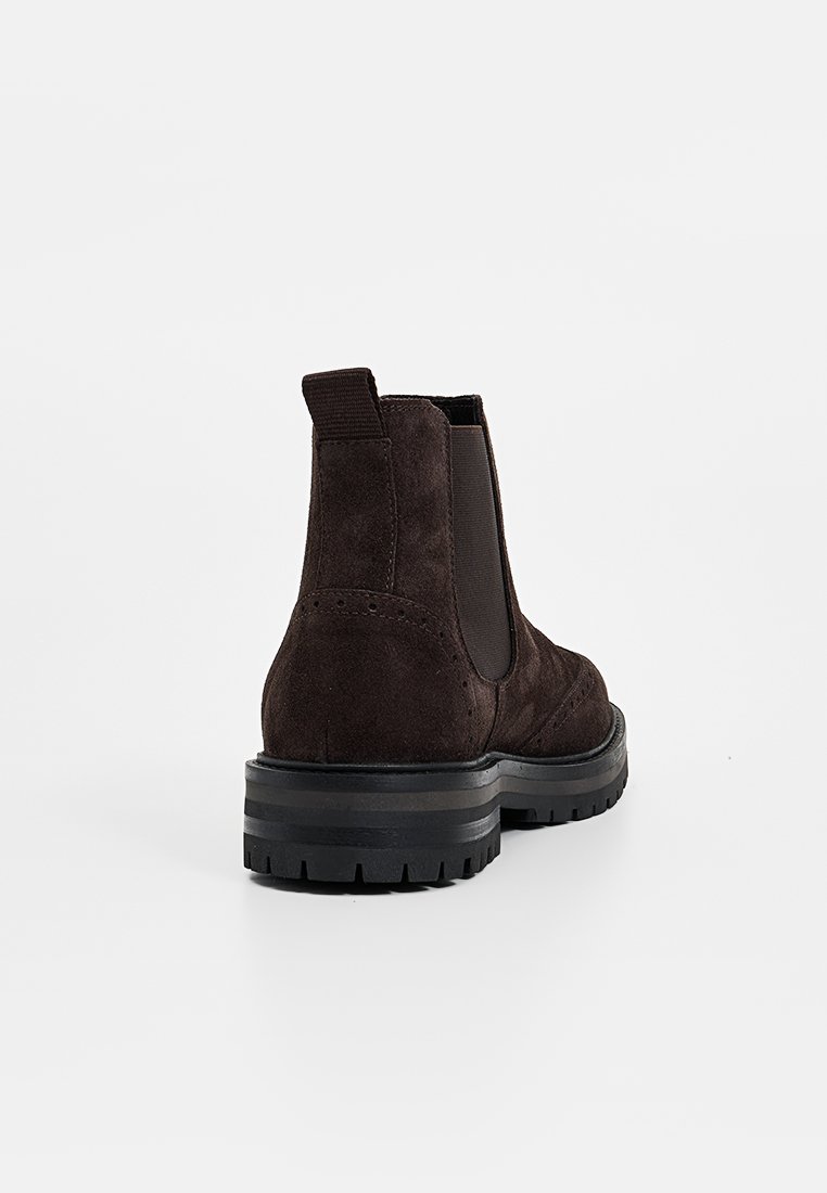 Braune Wildleder-Stiefeletten mit elastischen seitlichen Einsätzen und einer robusten schwarzen Gummisohle. Mit Nahtdetails und einer Schlaufe an der Rückseite.