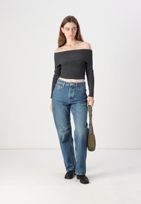 Top canelado cinza escuro, com alças caídas, combinado com jeans largos azul claro. Modelo segura uma bolsa verde oliva, posando contra um fundo simples.