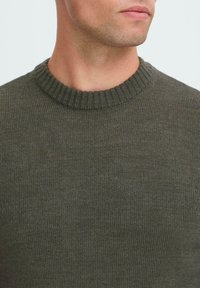 Dark green knitted sweater with a ribbed crew neckline, showcasing a smooth, textured fabric and fitted design.