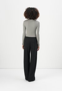 Ribbet grå langermet topp kombinert med høy midje, vide bukser med svarte pinstriper. Detaljene inkluderer to baklommer og tettsittende ermer.