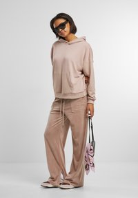 Lys rosa loungewear-set som inkluderer en løs hettegenser med frontlomme og matchende vide bukser. Glatt, myk stoff med en avslappet passform.