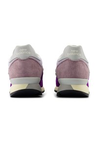 New Balance Sneaker mit einem Obermaterial aus lila und pinkem Wildleder, grauen Akzenten und einer weißen Fersenschlaufe mit Logo, auf einer cremefarbenen und schwarzen Sohle.