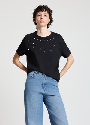Maglietta nera a maniche corte con scollatura arrotondata, decorata con un motivo di perle finte sul davanti. Abbinata a jeans di jeans blu.